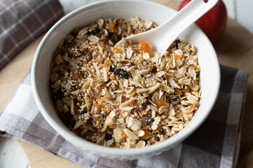 Homemade granola with oats, puffed amaranth, quinoa, almonds, dried fruits such as apricots, plums, apples, and dates in bowl with spoon