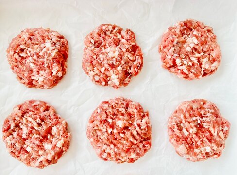 Overhead view of six raw minced pork and beef patties on parchment paper