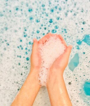 Close-up of a person with hands cupped holding soap suds in the bath