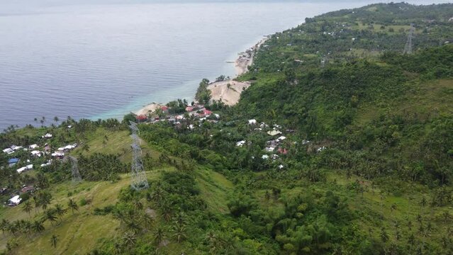 Electricity lines transmission towers above seaside village between tropical green coastal foothill terrain on Cebu island, Philippines. Aerial