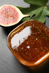 Glass bowl with tasty sweet jam, fresh fig and green leaf on grey table, above view
