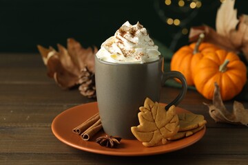 Tasty pumpkin spice latte with whipped cream in cup and cookies on wooden table, closeup