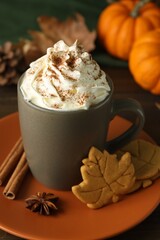 Tasty pumpkin spice latte with whipped cream in cup and cookies on table, closeup
