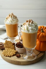 Tasty pumpkin latte with whipped cream in glasses, spices and cookies on white wooden table