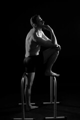 Front and side view photo of an strong young man exercising on parallel bars in studio.