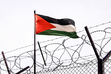 View of palestinian flag behind barbed wire against cloudy sky. A border post on the border of...