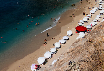 A big red umbrella. A distant view of one of Antalya's famous bays with crowded beach and a big red umbrella.