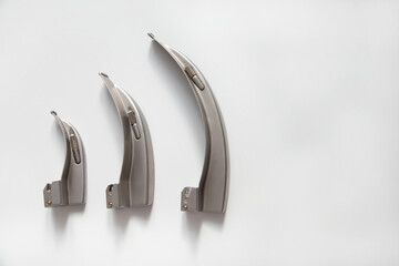 There are curved blades for a laryngoscope on a white table. Copy space.