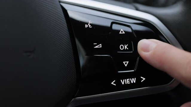 Close-up view of car interior. View of steering wheel of car control music. Driver pressing volume button of car radio on steering wheel of a car. Turns up the volume of the music in the car