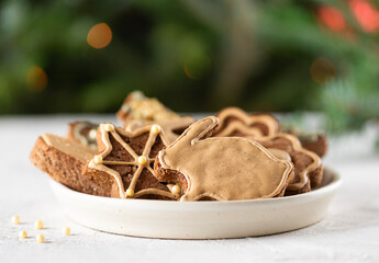 Vegan gingerbread cookies with honey, spices and aquafaba glaze in a plate on the background of a Christmas tree.