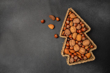a set of nuts in a Christmas tree shaped basket on a dark background, banner, menu, recipe place...