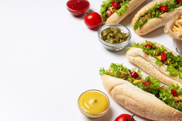 Hot dogs and sauces in bowls on white background, space for text