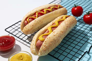 Hot dogs, sauces in bowls and tomatoes on white background, close up