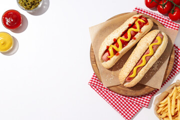 Hot dogs, sauces in bowls, french fries and tomatoes on white background, space for text
