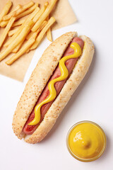 Hot dog, sauce in bowl and french fries on white background, top view