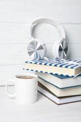 Cup of tea and headphones on stack of books on white wooden background