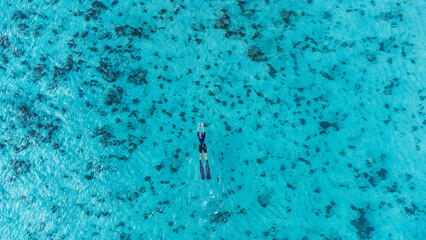 Stunning aerial view of a young woman swimming with carbon fins and wetsuit in turquoise waters over a vibrant coral reef © Alex Pelikh