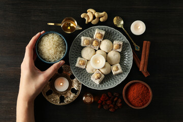 Sweets, spices, rice, candles and hand on dark wooden background, top view