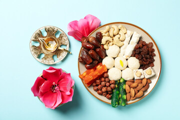 Plate with sweets, copper utensils and flowers on blue background, top view