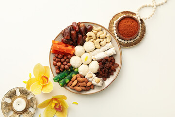 Plate with sweets, candle, flowers and spices on white background, top view