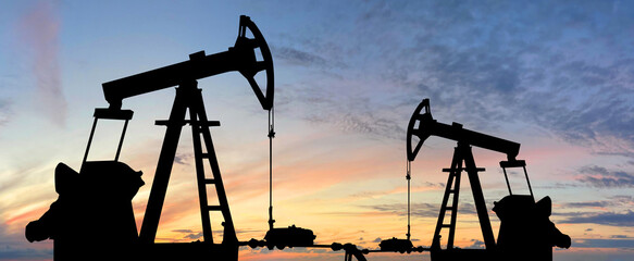 Oil pump jack. Oil industry equipment rig silhouette against sunset sky clouds background