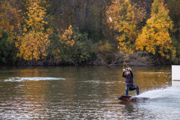 Fototapeta na wymiar Girl on a wakeboard. An athlete performs a trick on the water. Autumn Park