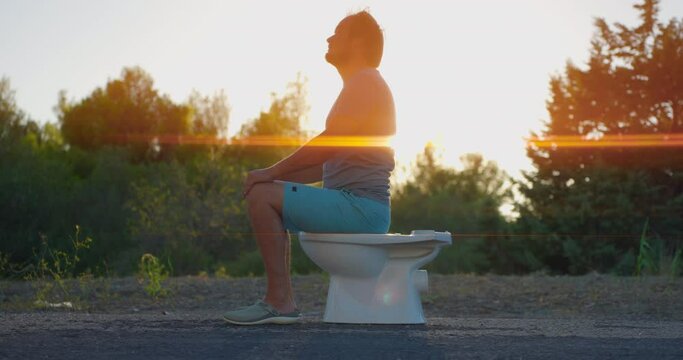 The man sit in the toilet on the background of sunset