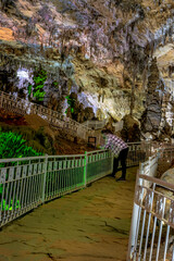 Beni Add cave, Ain Fezza, Tlemcen, Algeria. Interior view with its marvelous colorful stalagmites and stalactites. White ramp for the pedestrian walkway path. A man is leaning on the railing.