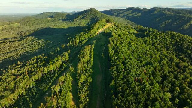 the drone on the left flies around the top of the mountain on which the ski slopes and lifts are located, opening an amazing mountain landscape. Summer, evening. Ukrainian Carpathians, Myhove village.