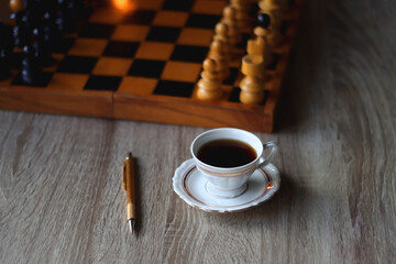 Vintage wooden chessboard, books, glasses, pen, cup of tea or coffee and scented candle on the...