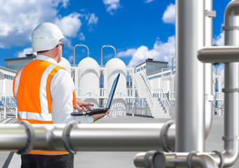 Chemical industry. Engineer near factory. Man factory technologist with his back to camera. Chemical plant engineer with laptop. Employee near industrial structures. Man and industrial tanks