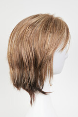 Natural looking dark brunet wig on white mannequin head. Short brown hair on the plastic wig holder isolated on white background, side view.