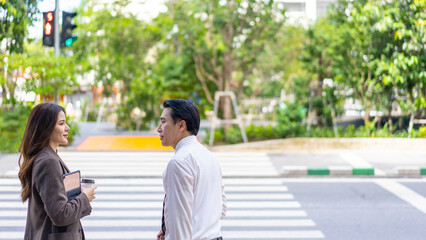 Confidence Asian businessman and businesswoman office worker holding briefcase and laptop computer walking street crosswalk in the city. Business people company employee go to work in the morning.