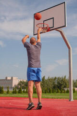 A young man throws a ball into a basketball basket while playing on an outdoor playground on the street