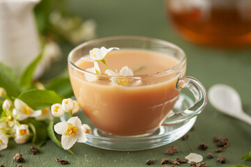 Composition with cup of jasmine milk tea and flowers on green background