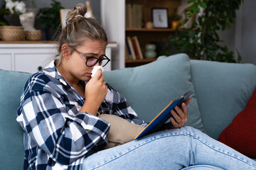 Sad woman crying while she reading a good paper book sitting on a sofa at home. Upset girl read...