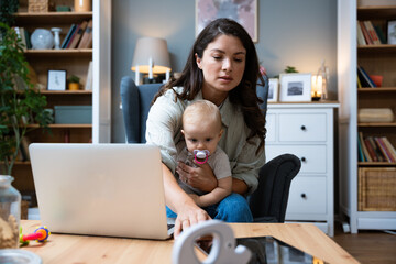 Young female business owner work on laptop from home during maternity leave, running private company with baby in her lap. Businesswoman mother woman with a toddler working at the computer. - obrazy, fototapety, plakaty