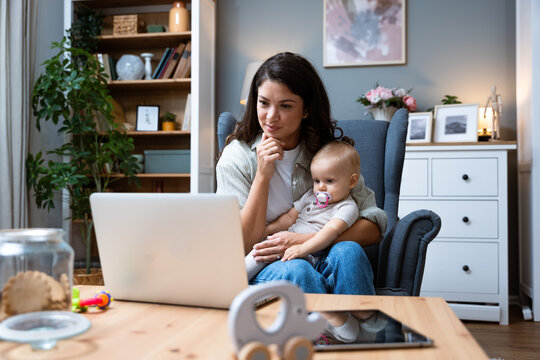 Young female business owner work on laptop from home during maternity leave, running private company with baby in her lap. Businesswoman mother woman with a toddler working at the computer.