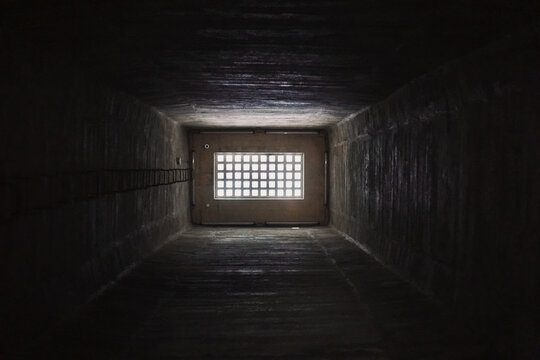 Light behind barred window in the dark prison cell - empty jail interior with grey concrete walls