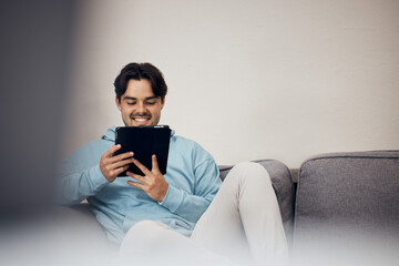 Happy man, tablet and relax on sofa for social media, communication or entertainment in living room at home. Male person, smile and lying on lounge couch with technology for online streaming at house