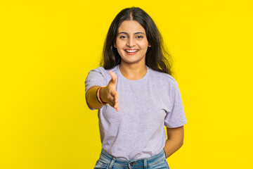 Naklejka premium Friendly Indian young woman outstretching hand to camera, offering handshake greeting with kind smile invitation, welcoming showing solidarity trust concept. Arabian girl isolated on yellow background