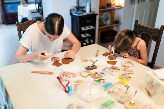 Culinary workshops for children. Two sisters decorating gingerbread cookies at home in the kitchen. 