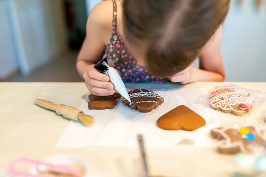 Little girl decorating gingerbread cookies with icing sugar. Selective focus.