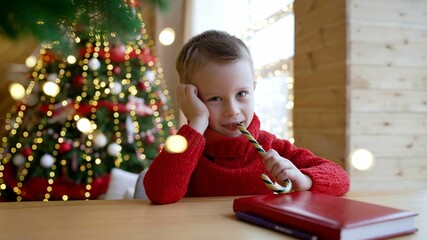 A little boy in a Christmas sweater in an interior with a Christmas tree and gifts. Waiting for...