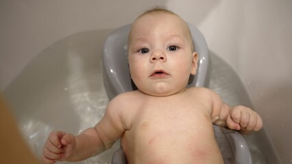 Portrait of an adorable cute baby taking his first bath and smiling. Bathing a newborn in a tub. First days of life. A little boy takes a bath for the first time.