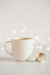 A white cup with hot coffee or tea on a white wooden table with Christmas lights.