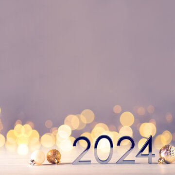 Metal numbers 2024 on a white table with Christmas decorations and bokeh lights. Happy New Year 2024 is coming concept.