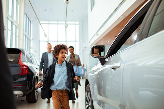 Excited young boy looking at cars with his parents behind him at the dealership