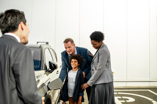 Young interracial family charging their new electric car at the dealership parking lot