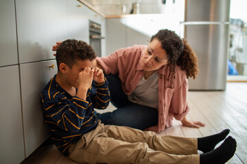 Young mixed mother comforting her crying son on the floor at home